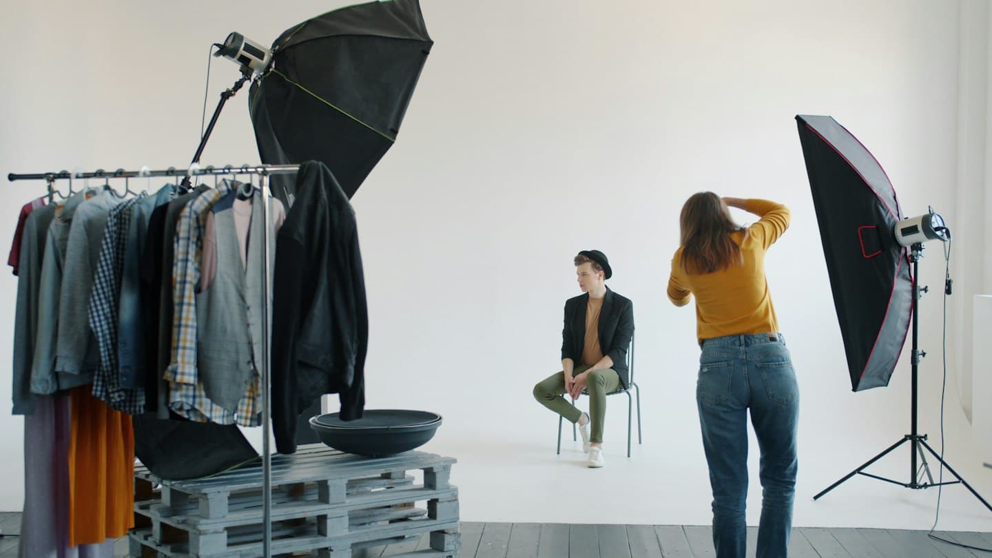 Fotógrafo dirige a modelo masculino en un estudio minimalista.